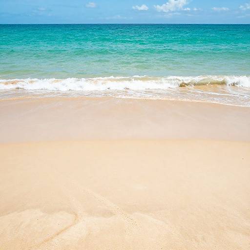 Photograph of a serene beach with golden sand, gentle turquoise waves, and a clear blue sky with scattered clouds.