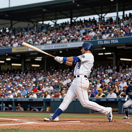 Photograph of a baseball player in a white and blue uniform hitting a ball, with a crowded stadium in the background. Player wears number 9,