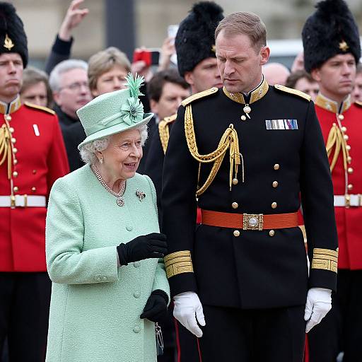 Photograph of elderly Queen Elizabeth II in light green outfit and hat, smiling, beside a male military officer in black uniform with gold details. Background: