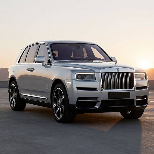 Photograph of a sleek silver Rolls-Royce sedan with black rims, parked on a sunlit concrete surface at sunset.