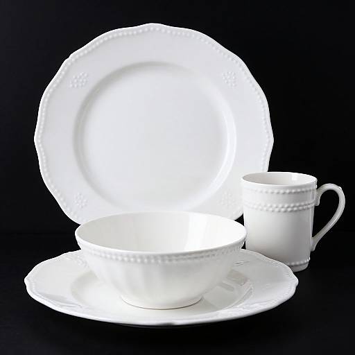 Photograph of a glowing white porcelain teacup, saucer, and large plate against a black background, with intricate bead-like patterns.