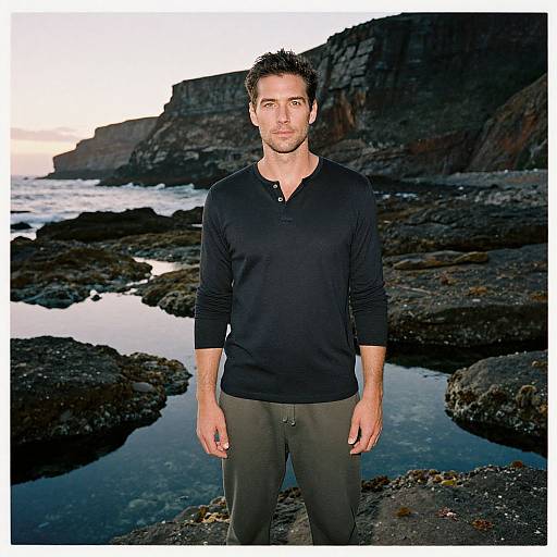 Man Standing on Rocky Ocean Shoreline at Sunset
