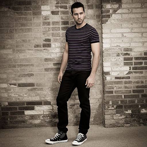 Man in Striped T-Shirt and Black Jeans Against Brick Wall