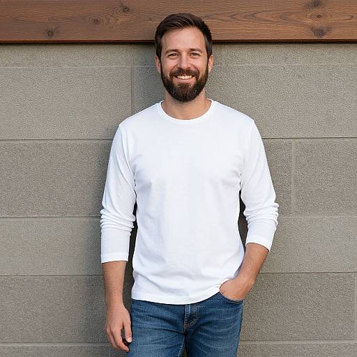 Smiling Man in White Long Sleeve Shirt and Jeans Against Gray Wall