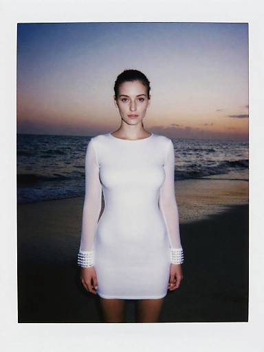 Woman in Minimalist White Shift Dress with Sheer Sleeves at Beach Sunset
