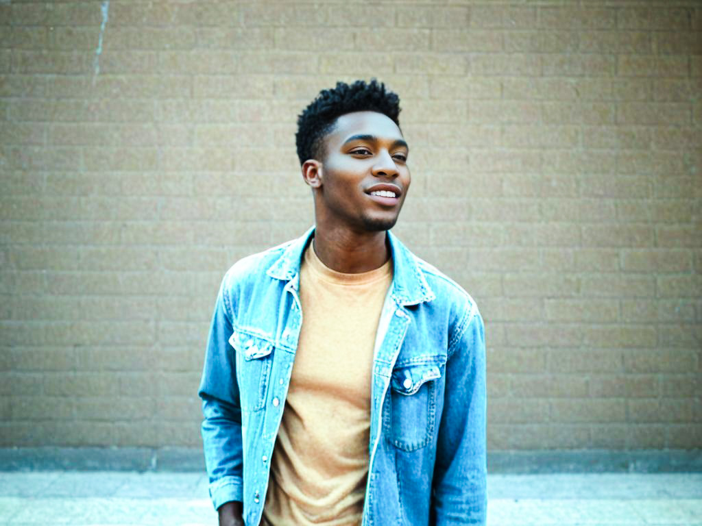 Stylish Young Man in Denim Jacket Against Brown Wall