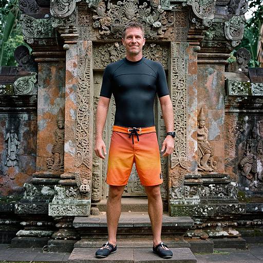 Man in Orange Swim Shorts Posing at Ornate Stone Temple