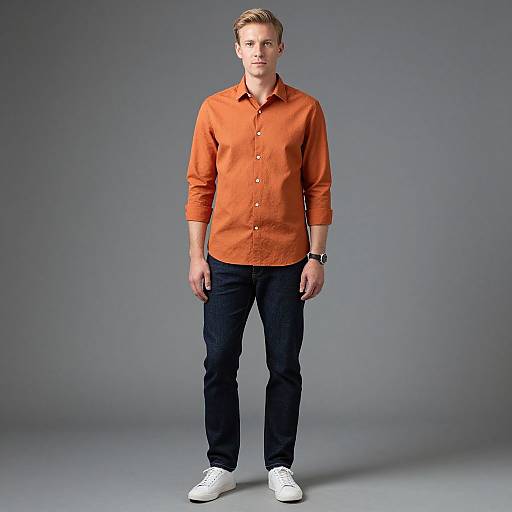 Casual Young Man in Orange Shirt and Dark Jeans Standing on Gray Background