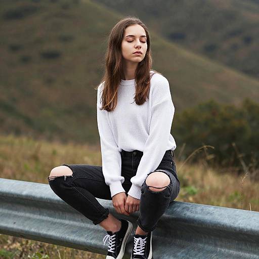 Contemplative Young Woman Sitting on Guardrail in White Sweater and Ripped Jeans