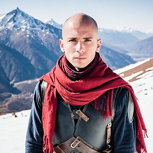 Man in Dark Armor and Red Scarf in Snowy Mountains