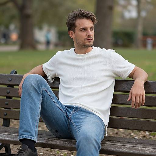 Young Man Sitting on Park Bench in Casual White Sweater and Jeans