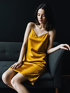 Elegant Woman in Mustard Yellow Satin Slip Dress Sitting on Gray Sofa