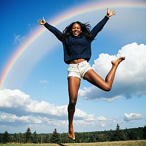 Joyful woman jumping with rainbow and blue sky