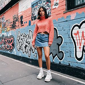 Trendy Young Woman in Coral Sweater and Denim Skirt Against Graffiti Wall