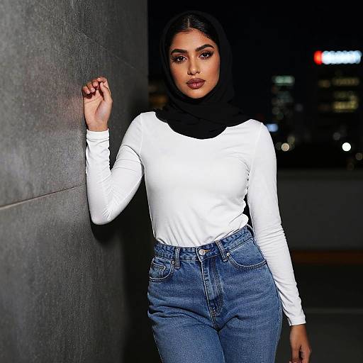 Confident Woman in Black Hijab and White Top Posing Against Night Cityscape
