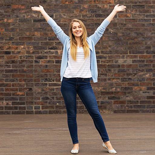 Happy Young Woman Celebrating with Raised Arms Against Brick Wall