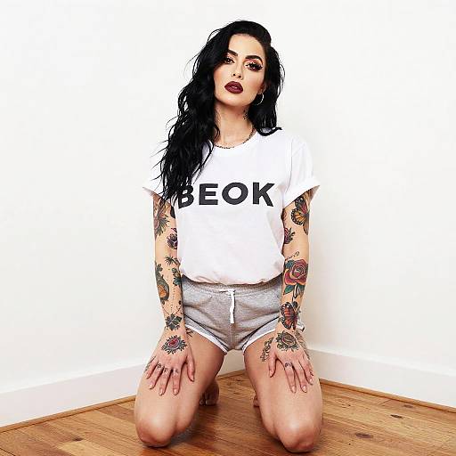 Tattooed Woman in Casual Outfit Wearing BEOK T-Shirt Kneeling on Wooden Floor