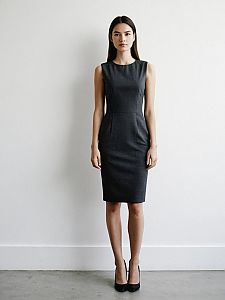 Professional Woman in Sleek Charcoal Gray Sheath Dress Standing Against White Wall