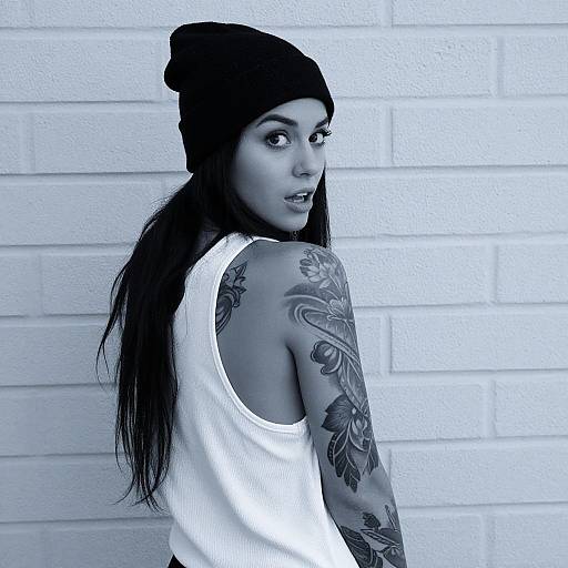 Tattooed Woman in Beanie and White Tank Top Against Brick Wall