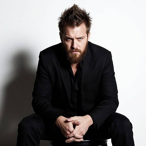 Serious Bearded Man in Black Suit Sitting on Stool