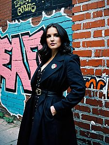 Confident Woman in Black Coat Posing by Graffiti Brick Wall Urban Fashion Portrait