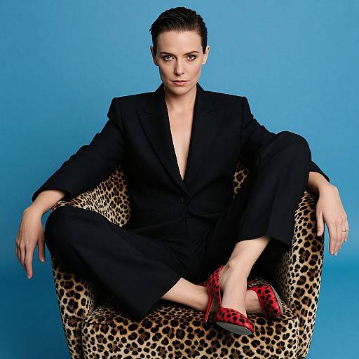 Confident Woman in Black Suit Sitting on Leopard Print Chair with Red Heels
