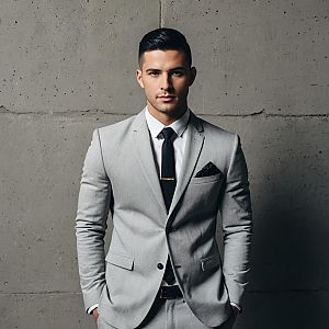 Stylish Man in Light Gray Suit Wearing Black Tie Against Concrete Wall