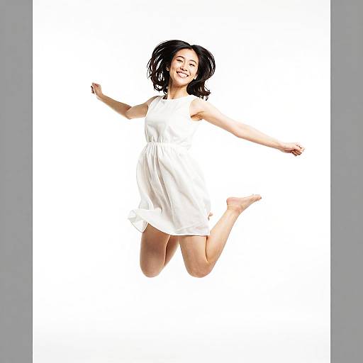 Joyful Young Woman Jumping in White Dress on White Background