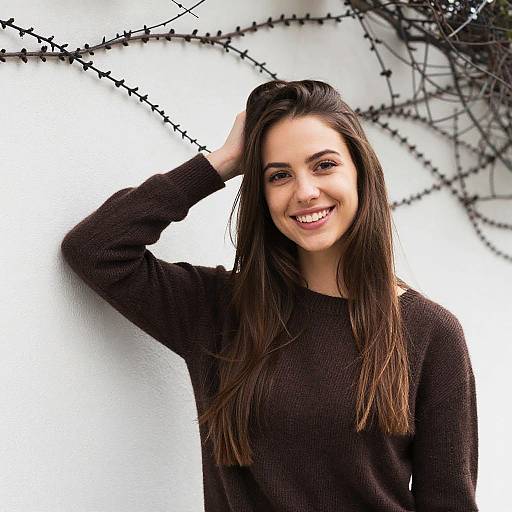 Smiling Young Woman in Brown Sweater Standing by Vine-covered Wall